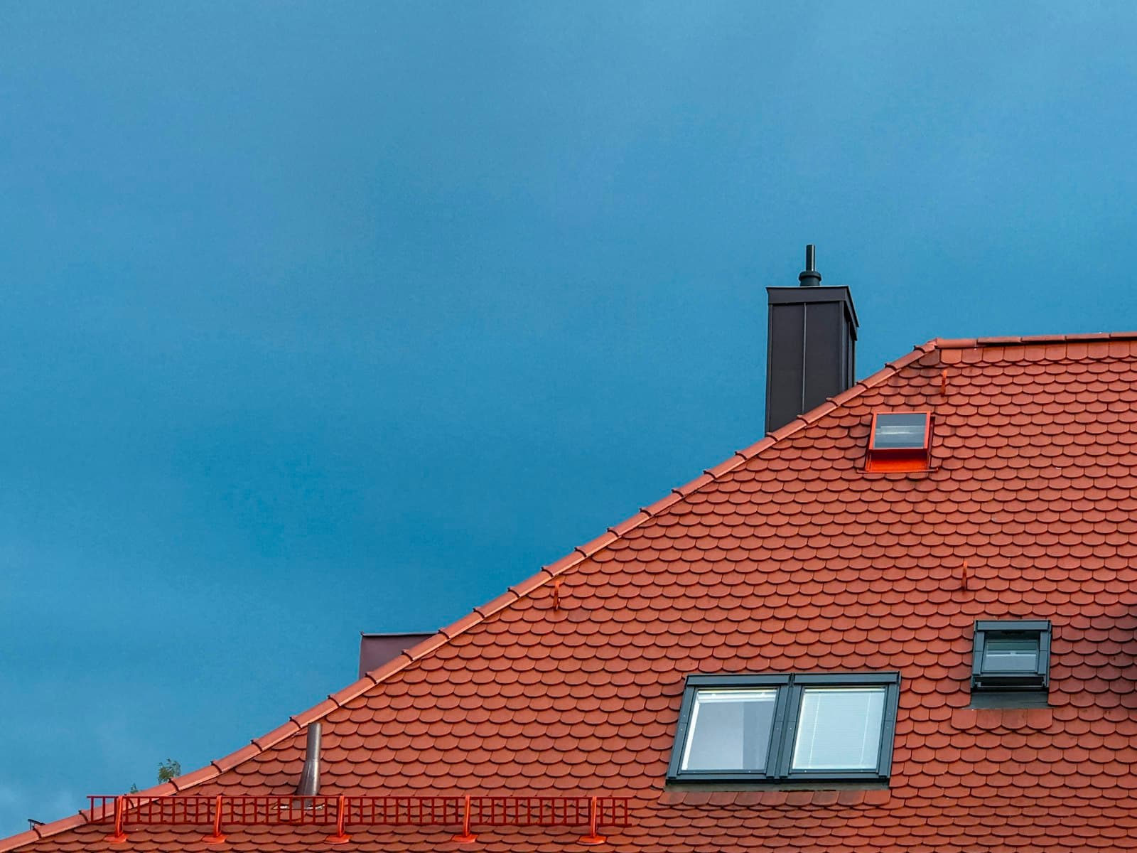 Terracotta tiled roof with a chimney against a stormy sky