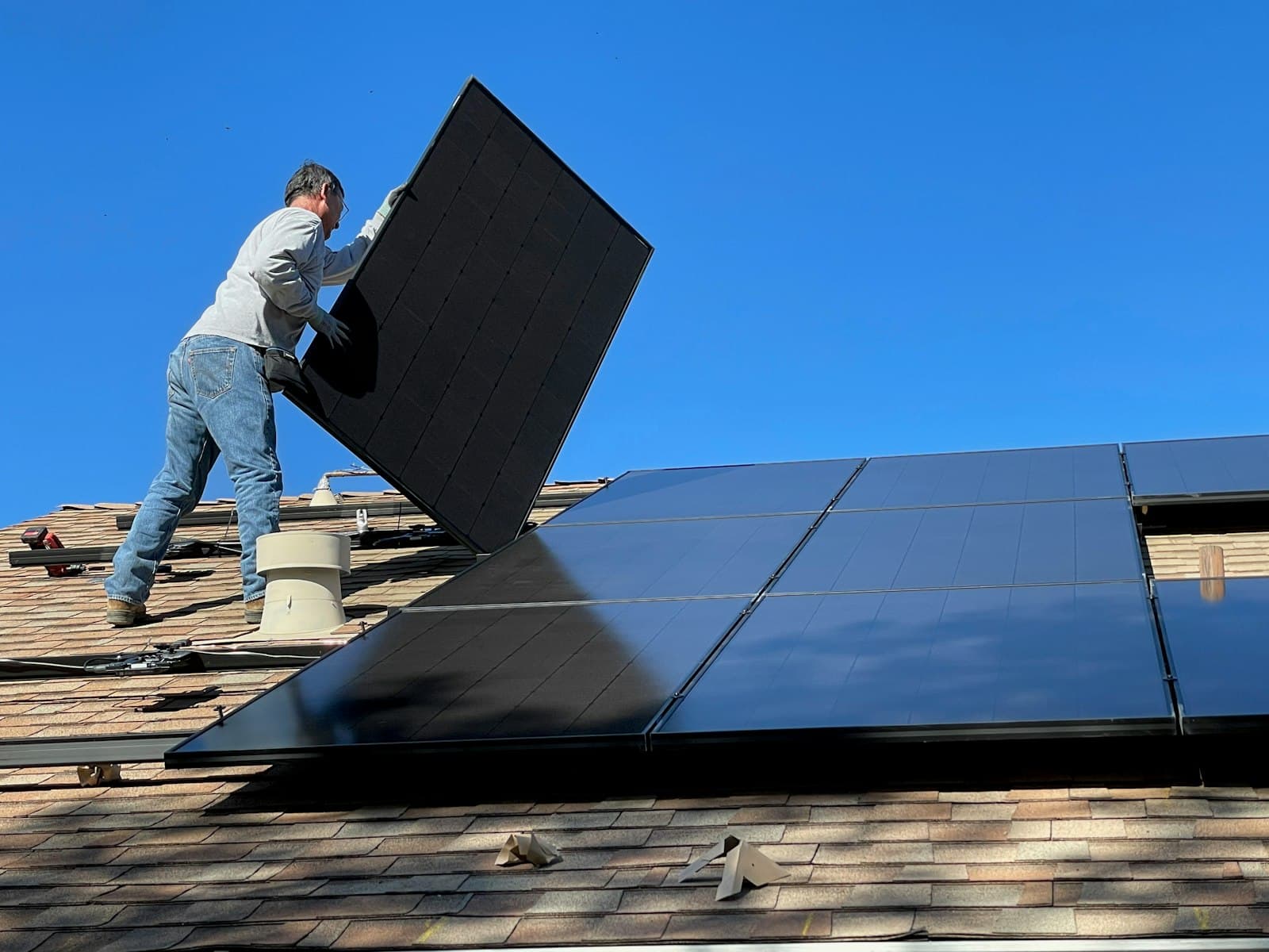 Installer positioning a solar panel on a roof under a blue sky