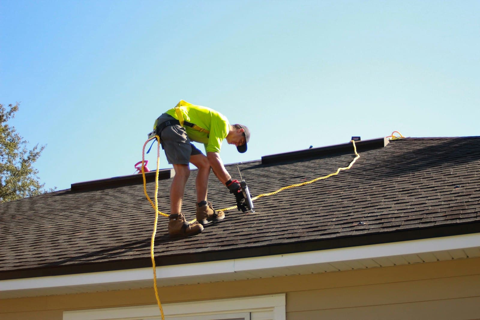 Roofer in hi-vis kneeling on a roof while fixing it with a power drill